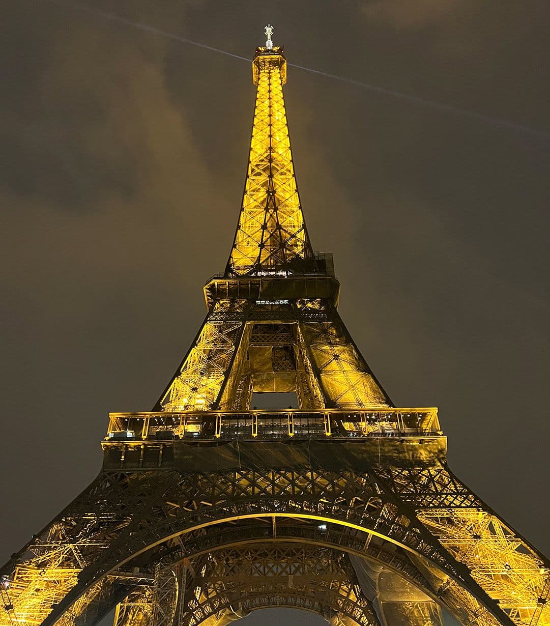 The Eiffiel Tower, a huge metal towering structure illuminated at night with a cloudy sky.
